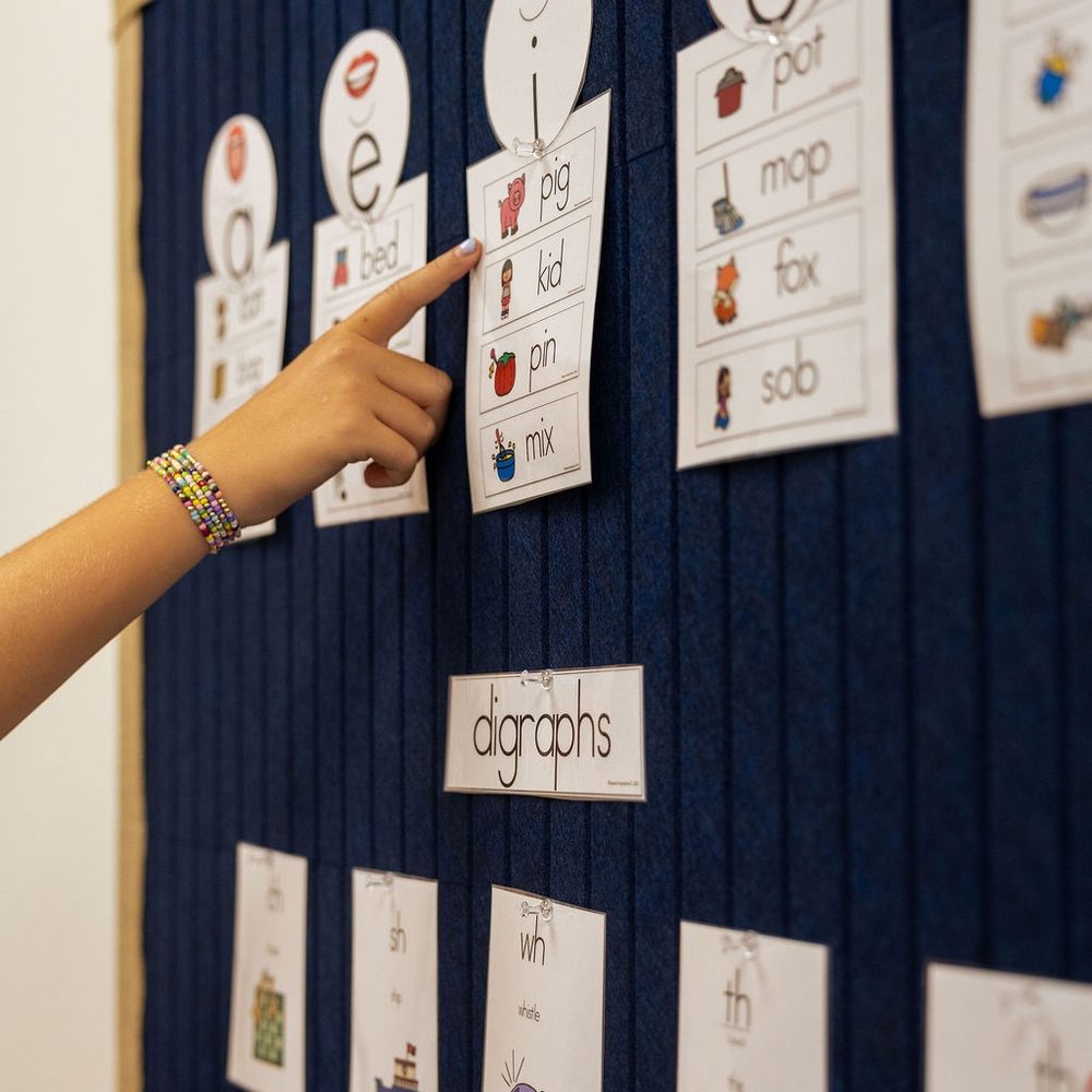 A child points to a digraph card on the classroom sound wall