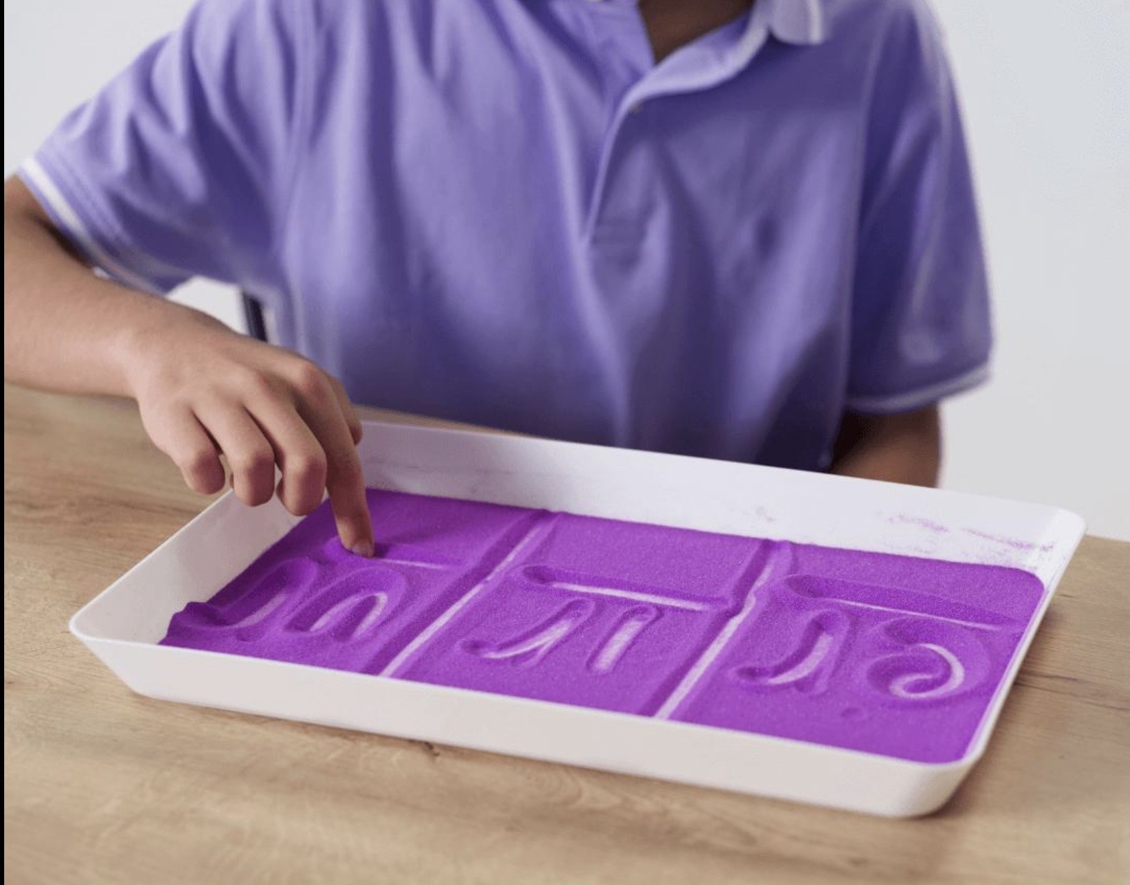 A child traces letters in a sand tray, a multisensory Orton-Gillingham technique