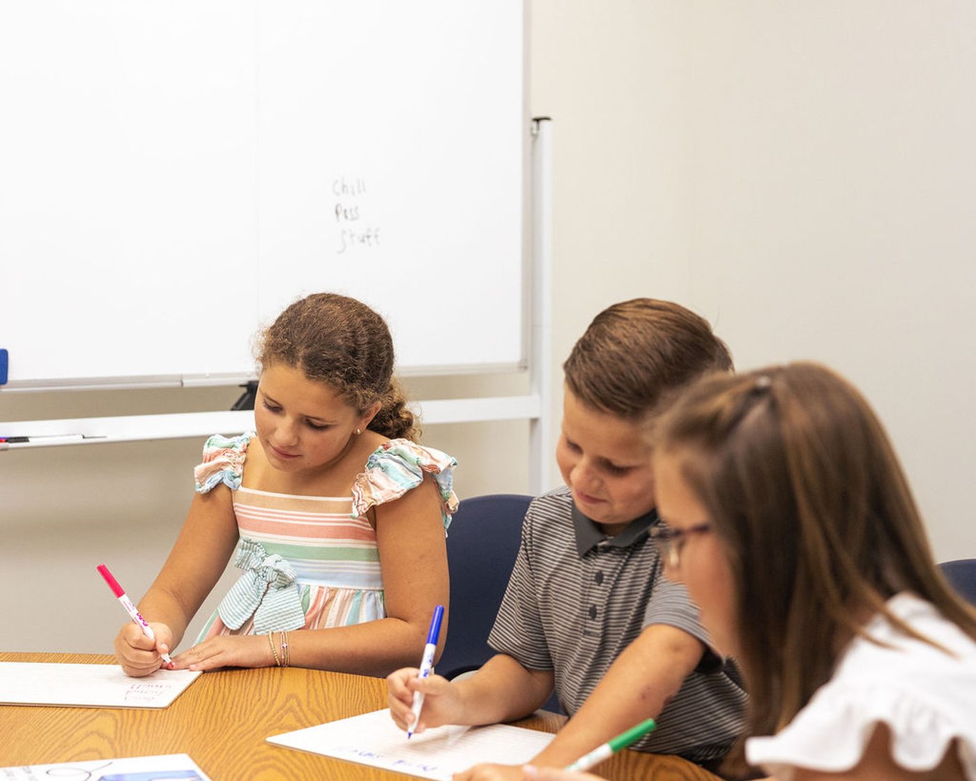 Three children write at a shared table during a small-group literacy lesson