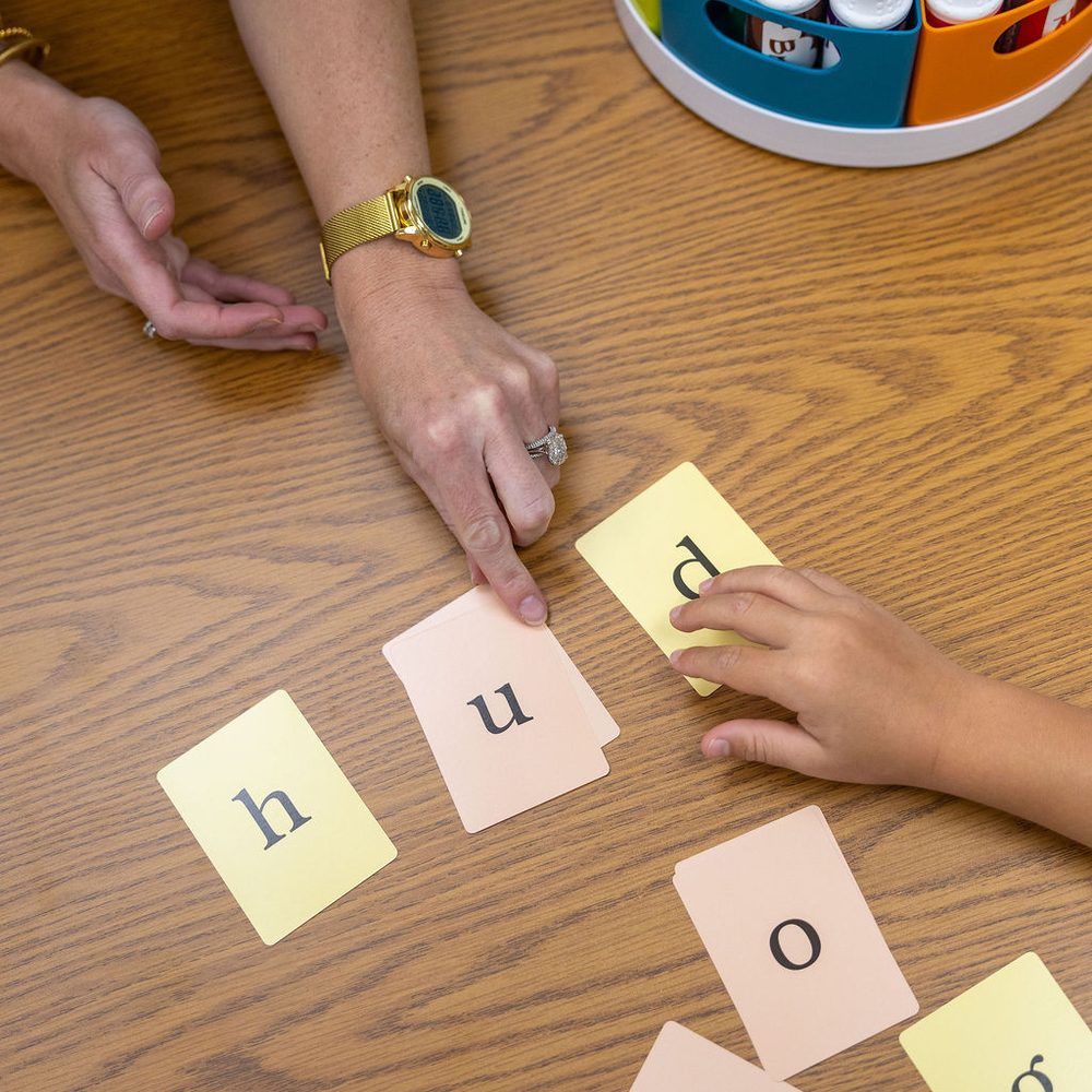 A child arranges letter tiles to build a word while a teacher guides the lesson