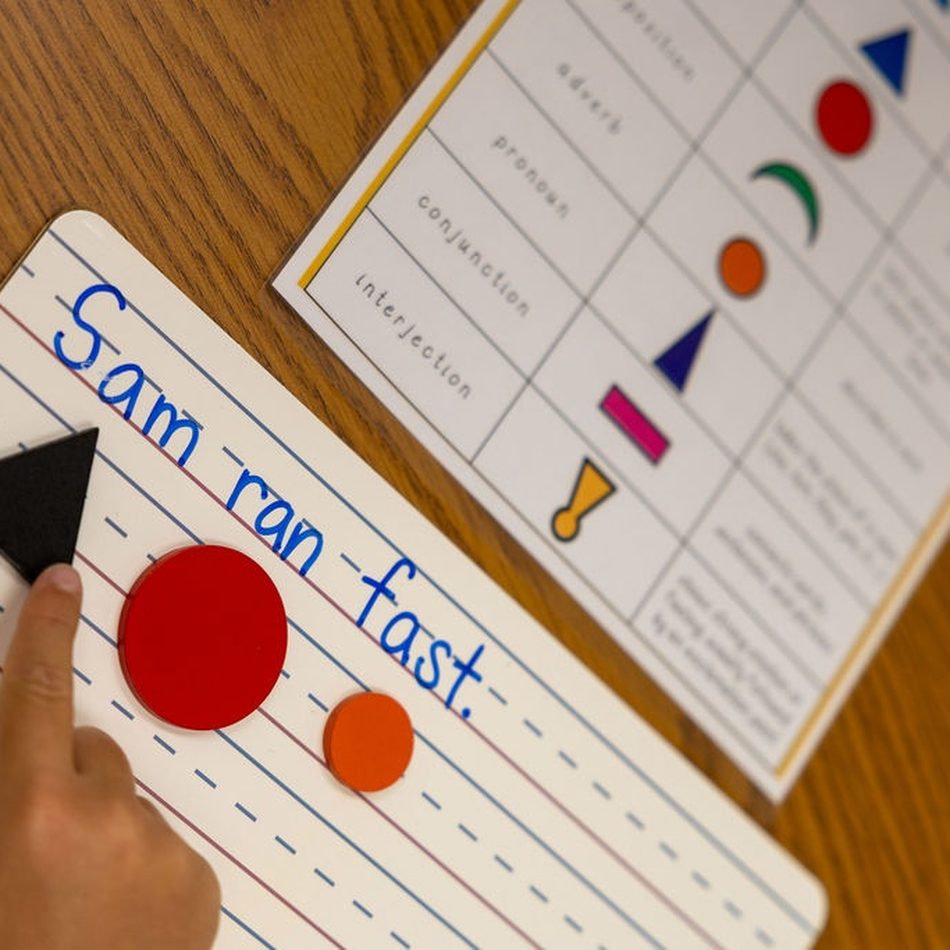 A child writes the sentence “Sam ran fast” on a lined practice board