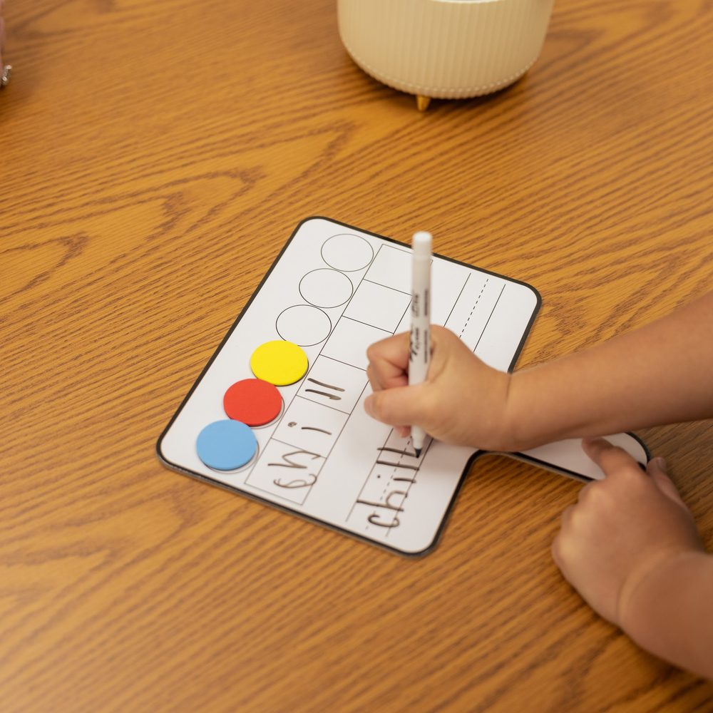 A child writes a word on a magnetic sound board with a marker